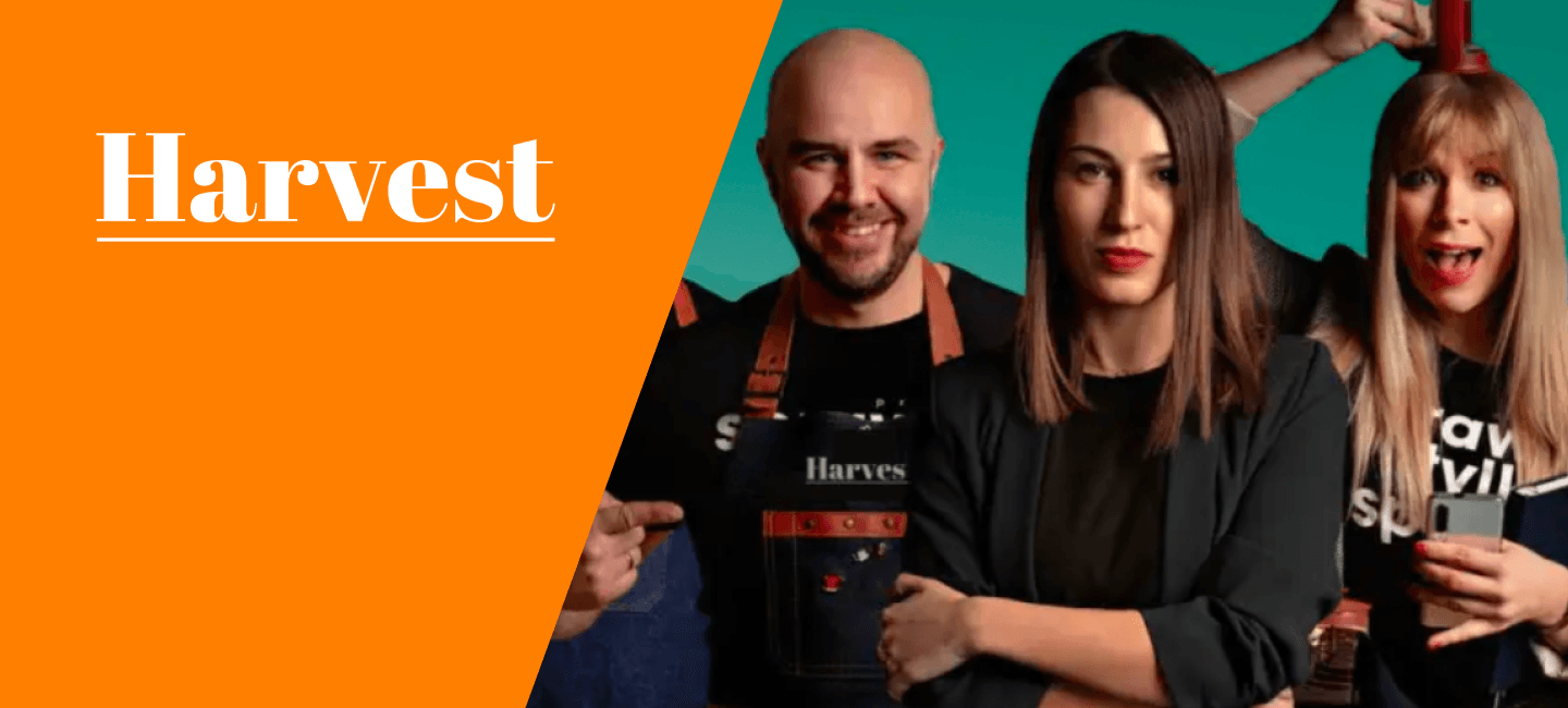 Pozioma grafika promocyjna marki Harvest, podzielona ukośną linią na dwie części. Po lewej stronie znajduje się jednolite, intensywnie pomarańczowe tło z dużym, białym napisem „Harvest”, podkreślonym cienką linią. Po prawej stronie widoczna jest grupa trzech osób na turkusowym tle. Na pierwszym planie stoi kobieta z długimi, prostymi, brązowymi włosami, ubrana w czarny strój. Obok niej znajduje się łysy mężczyzna z krótką brodą, ubrany w czarną koszulkę i fartuch z napisem „Harvest”. Po prawej stronie stoi blondynka z grzywką, ubrana w czarną koszulkę z białym napisem i trzymająca w dłoni smartfon. Nad grupą widoczna jest uniesiona dłoń trzymająca czerwony element. Grafika przedstawia markę Harvest i jej zespół w dynamicznej, kolorowej aranżacji.
