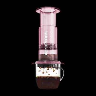 Zdjęcie różowego zaparzacza AeroPress Clear Pink, umieszczonego na szklance z zaparzaną kawą. Widoczna jest ekstrakcja kawy, której krople spadają do kubka, ukazując proces parzenia kawy metodą AeroPress.