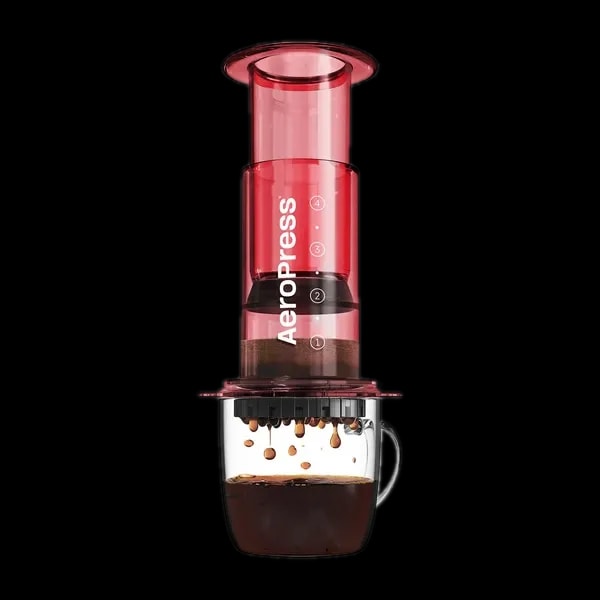 Zdjęcie czerwonego zaparzacza AeroPress Clear Red, umieszczonego na szklance z zaparzaną kawą. Krople kawy spadają do kubka, pokazując proces parzenia metodą AeroPress, z przezroczystym czerwonym korpusem urządzenia.