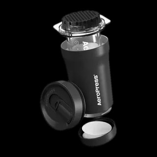 Zdjęcie AeroPress Go Plus w kolorze czarnym, pokazujące kompaktową formę zestawu podróżnego. Widoczny jest AeroPress z pokrywką, sitko oraz pojemnik na filtry, idealny do łatwego przechowywania i transportu.