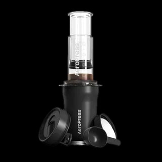 Zdjęcie AeroPress Go Plus w kolorze czarnym, prezentujące pełny zestaw do parzenia kawy, w tym prasa AeroPress, czarna miarka, pokrywka oraz pojemnik do przechowywania. Zestaw przeznaczony do łatwego przygotowywania kawy w podróży.