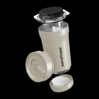 Zdjęcie złożonego zestawu AeroPress Go Plus w kolorze kremowym, w którym widoczna jest cylindryczna komora do parzenia kawy, przykryta nakładką z sitkiem, obok leży zamknięcie podróżne oraz pojemnik na filtr papierowy. Kompaktowy zestaw idealny do przygotowywania kawy w podróży.