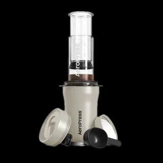 Zdjęcie kremowego ekspresu AeroPress Go Plus, w skład którego wchodzi cylindryczna komora do parzenia kawy, tłok z miarką, pokrywka podróżna oraz miarka do kawy. Urządzenie jest kompaktowe i idealne do przygotowywania kawy w podróży.