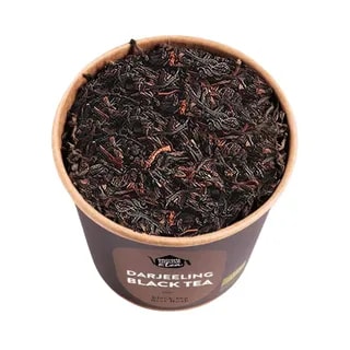 Ekspresyjny widok czarnej herbaty Darjeeling w papierowym pojemniku, ukazujący mieszankę liści o intensywnym kolorze. Idealna dla miłośników herbaty, oferująca bogaty smak i aromat, doskonała do parzenia w domowym zaciszu lub na wyjątkowe okazje.