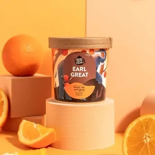 Opakowanie herbaty Earl Great przedstawia aromatyczną mieszankę czarnej herbaty Earl Grey z nutą kokosa i wanilii. Kompozycja jest umieszczona na pastelowym tle w towarzystwie świeżych pomarańczy, co podkreśla jej orzeźwiający charakter idealny na każdy dzień.