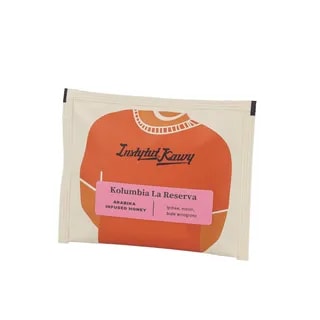 Drip bag z kawą Kolumbia La Reserva od Instytutu Kawy. Opakowanie z grafiką pomarańczowego swetra i różową etykietą. Profil smakowy: lychee, melon, białe winogrono. Arabika w obróbce infused honey.