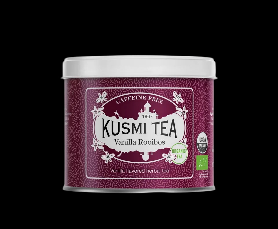 Fioletowa puszka herbaty Kusmi Tea Vanilla Rooibos z napisem "Caffeine Free" i "Organic Tea." Zawiera herbatę rooibos o smaku waniliowym, z certyfikatem USDA Organic oraz unijnym certyfikatem ekologicznym. Elegancki design z białymi zdobieniami i motywem wanilii.