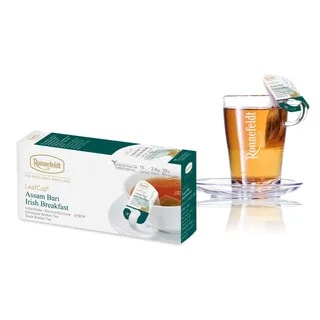 Opakowanie herbaty Ronnefeldt LeafCup Assam Bari Irish Breakfast obok szklanki z przygotowaną herbatą. Herbata Assam Bari Irish Breakfast to czarna herbata z mieszanką przypraw, oferowana w eleganckim pudełku z 15 torebkami herbaty, idealna do przygotowania aromatycznego napoju. Obok znajduje się przezroczysta szklanka z logo Ronnefeldt, ukazująca napój o bogatej, ciemnej barwie.