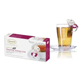 Opakowanie herbaty Ronnefeldt LeafCup Darjeeling Summer Gold obok szklanki z przygotowaną herbatą. Herbata Darjeeling Summer Gold to czarna herbata z mieszanką przypraw, oferowana w eleganckim pudełku z 15 torebkami herbaty, idealna do przygotowania aromatycznego napoju. Obok znajduje się przezroczysta szklanka z logo Ronnefeldt, ukazująca napój o bogatej, ciemnej barwie.