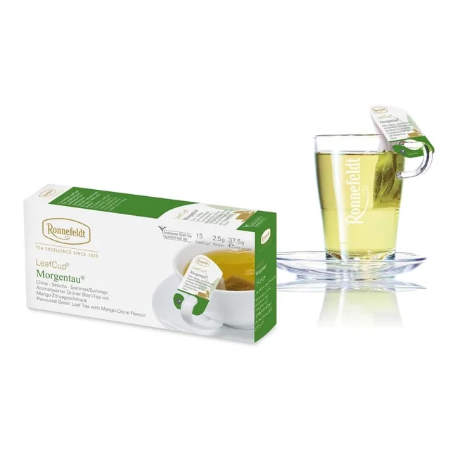 Opakowanie herbaty Ronnefeldt LeafCup Morgentau obok szklanki z przygotowaną herbatą. Herbata Morgentau to czarna herbata z mieszanką przypraw, oferowana w eleganckim pudełku z 15 torebkami herbaty, idealna do przygotowania aromatycznego napoju. Obok znajduje się przezroczysta szklanka z logo Ronnefeldt, ukazująca napój o bogatej, ciemnej barwie.