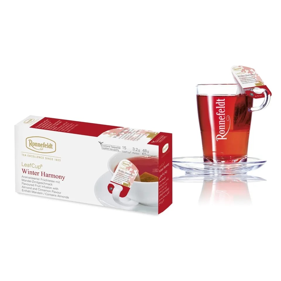 Opakowanie herbaty Ronnefeldt LeafCup Winter Harmony, zawierające 15 saszetek aromatyzowanej herbaty owocowej o smaku migdałów i cynamonu, każda o wadze 3,2 g (48 g netto). Obok znajduje się filiżanka z gorącą herbatą z logo Ronnefeldt na szklance oraz etykietą 'Winter Harmony'. Opakowanie utrzymane w białych i czerwonych tonacjach z motywem zimowym.