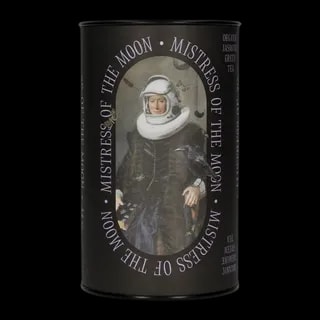 Puszka herbaty zielonej Leaf Liturgy „Mistress of the Moon” o smaku jaśminowym. Czarne opakowanie w kształcie cylindra ozdobione surrealistyczną grafiką kobiety w renesansowym stroju i hełmie astronauty, z krukiem siedzącym na ręce i unoszącymi się wokół motylami. Herbata organiczna, waga 60 g.