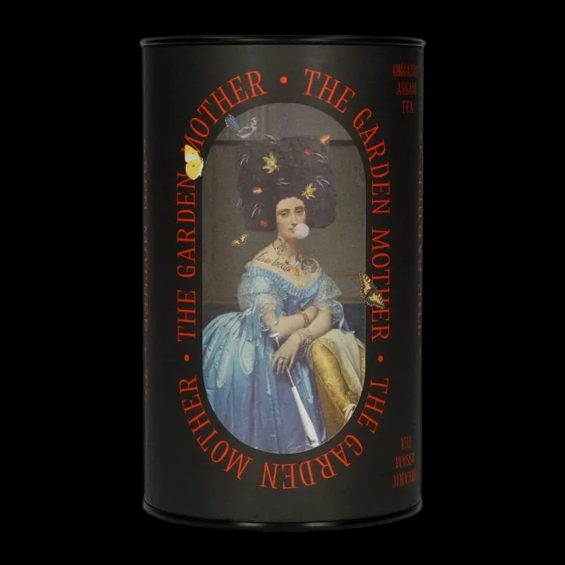 Herbata czarna Assam Leaf Liturgy The Garden Mother w nietuzinkowej tubie z barokową ilustracją kobiety żującej gumę i ozdobionej kwiatami. Produkt zawiera organiczny liściasty Assam o głębokim, wyrazistym smaku, zamknięty w opakowaniu przyciągającym uwagę nowoczesnym designem.