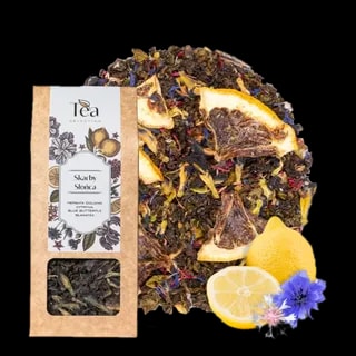 Opakowanie herbaty Skarby Słońca na białym tle, zawierającej mieszankę herbaty oolong, cytryny, blue butterfly oraz bławatera, obok talerz z suszonymi owocami i kwiatami, połowa cytryny, całe cytryny oraz niebieskie kwiaty chabra i białe kwiaty bławatera