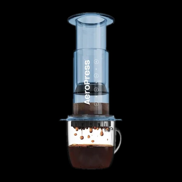 Zdjęcie niebieskiego zaparzacza AeroPress Clear Blue, umieszczonego na szklance z zaparzaną kawą. Krople kawy spadają do kubka, ukazując proces parzenia metodą AeroPress, z przezroczystym niebieskim korpusem urządzenia.