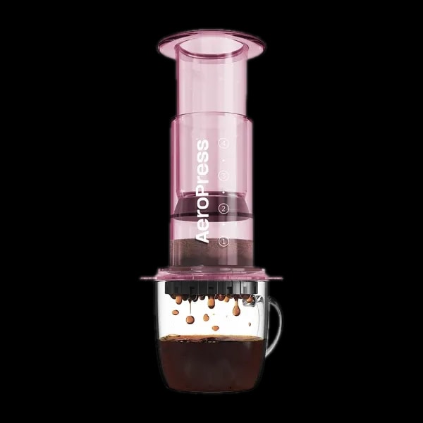 Zdjęcie różowego zaparzacza AeroPress Clear Pink, umieszczonego na szklance z zaparzaną kawą. Widoczna jest ekstrakcja kawy, której krople spadają do kubka, ukazując proces parzenia kawy metodą AeroPress.