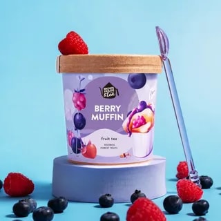 Na zdjęciu widoczny jest stylowy pojemnik z herbatą owocową Berry Muffin, który zawiera rooibos oraz leśne owoce. Obok pojemnika znajduje się świeża malina i borówki, co podkreśla wyjątkowy smak tego aromatycznego naparu, idealnego na każdą porę dnia.