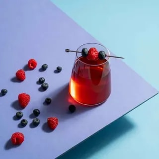 Szklanka aromatycznej herbaty udekorowanej świeżymi malinami i jagodami. Idealny napój na letnie dni, wzbogacający doznania smakowe każdego miłośnika herbaty.