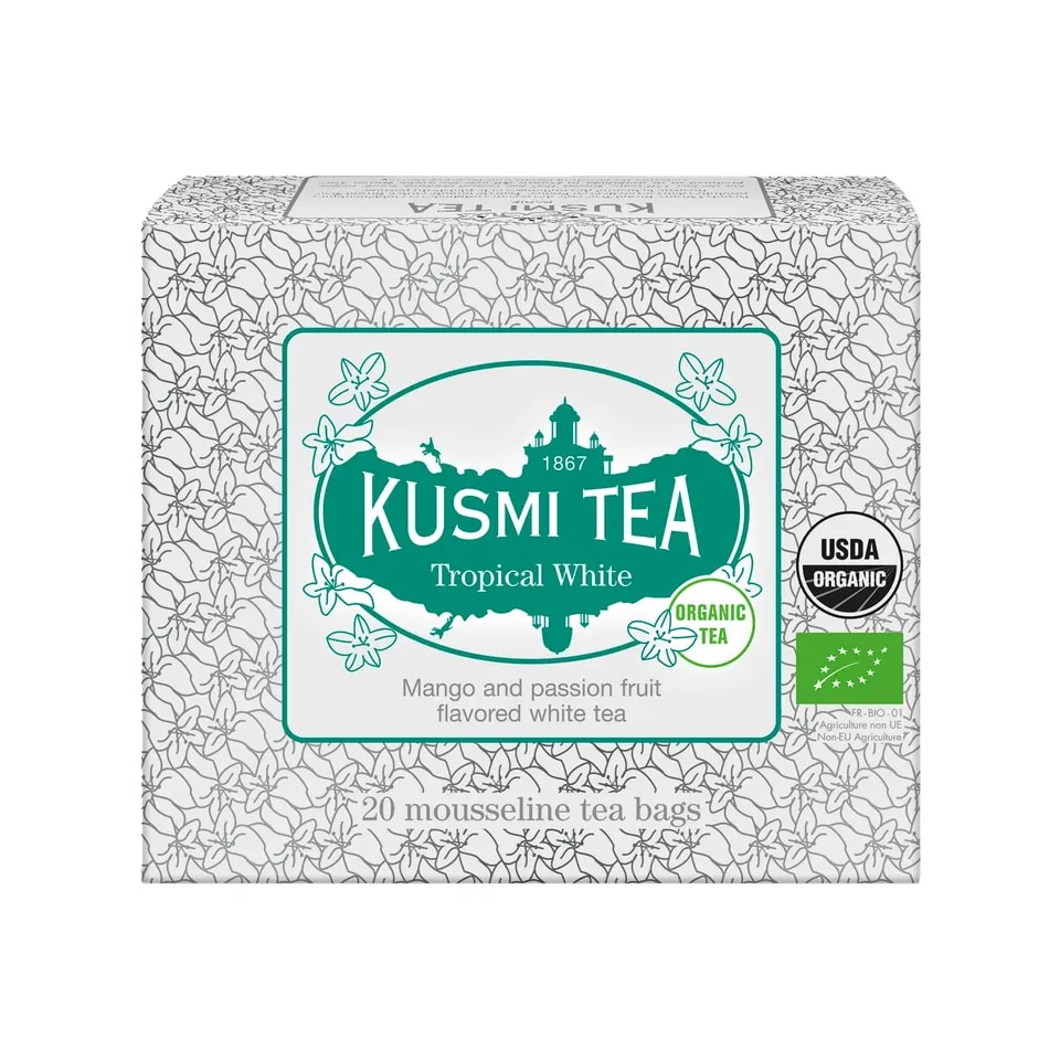 Kartonowe opakowanie herbaty Kusmi Tea Tropical White zawierające 20 saszetek, z ozdobną białą grafiką kwiatową i zielonym logo, oferujące organiczną białą herbatę o smaku mango i marakui.