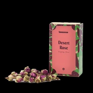 Opakowanie herbaty kwiatowej Teasome Desert Rose z regionu Xinjiang w Chinach, zawierające 50 g aromatycznych, suszonych pąków róż o intensywnie różowym kolorze. Produkt zaprezentowany jest w dekoracyjnym pudełku z motywem roślinnym, obok którego ułożono naturalne kwiaty przeznaczone do parzenia.