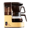 Ekspres przelewowy Melitta Aromaboy w kolorze beżowym, na białym tle. Kompaktowy design, idealny do parzenia 2 filiżanek kawy, wyposażony w szklany dzbanek, wskaźnik poziomu wody oraz funkcję automatycznego wyłączania