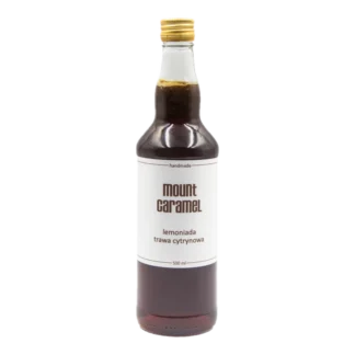 Średniej wielkości przezroczysta butelka z ciemną lemoniadą 'Trawa Cytrynowa' Mount Carmel, ręcznie robiona, o pojemności 500 ml, z białą etykietą informującą o smaku i marce