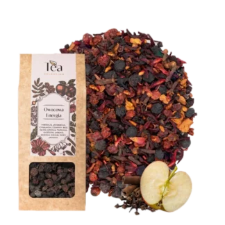 Opakowanie herbaty Owocowa Energia na białym tle, zawierającej mieszankę hibiskusa, jarzębiny, cynamonu, czarnego bzu, głogu, aronii, tarniny, goździków, jabłka, skórki dzikiej róży i jałowca, obok talerz z suszonymi owocami i przyprawami, pół jabłka, laska cynamonu oraz goździki