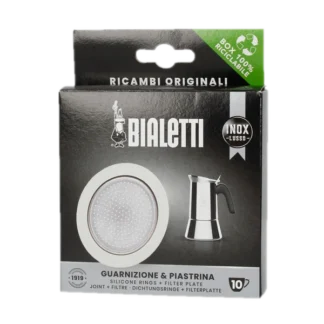 Opakowanie oryginalnego zestawu uszczelek i filtra do kawiarek stalowych Bialetti INOX LUSSO o rozmiarze 10 Tz. Produkt zawiera trzy silikonowe uszczelki oraz filtr z otworami, które są przeznaczone do kawiarek ze stali nierdzewnej Bialetti. Opakowanie w czarnym kolorze z białymi elementami, posiada logo Bialetti oraz zdjęcie kawiarki stalowej. Na górze opakowania widnieje informacja o 100% recyklingowalnym pudełku. Zestaw zapewnia wysoką jakość parzenia kawy i jest idealnym wyborem dla miłośników kawiarek Bialetti.