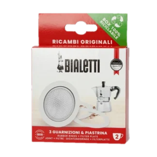 Opakowanie zawierające zestaw trzech uszczelek i sitko do kawiarek aluminiowych marki Bialetti, model 2 tz. Na zdjęciu widoczne jest pudełko z logiem Bialetti oraz rysunkiem kawiarki, a także informacją o zawartości - trzy gumowe uszczelki oraz metalowe sitko filtrujące. Zestaw przeznaczony do kawiarek aluminiowych, zapewnia dłuższą żywotność urządzenia oraz lepszą jakość parzenia kawy. Produkt jest zapakowany w ekologiczne opakowanie, w pełni nadające się do recyklingu.