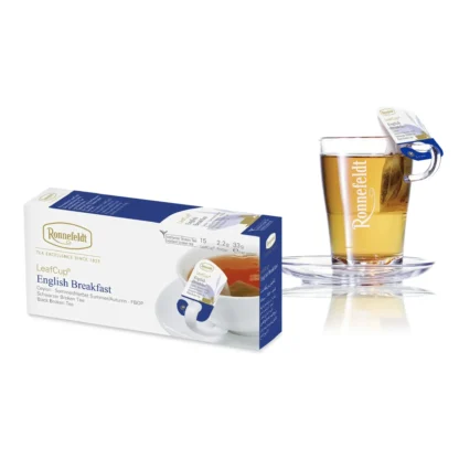 Opakowanie herbaty Ronnefeldt LeafCup EnglishBreakfast obok szklanki z przygotowaną herbatą. Herbata EnglishBreakfast to czarna herbata z mieszanką przypraw, oferowana w eleganckim pudełku z 15 torebkami herbaty, idealna do przygotowania aromatycznego napoju z mieszanką korzennych smaków. Obok znajduje się przezroczysta szklanka z logo Ronnefeldt, ukazująca napój o bogatej, ciemnej barwie.