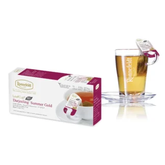 Opakowanie herbaty Ronnefeldt LeafCup Darjeeling Summer Gold obok szklanki z przygotowaną herbatą. Herbata Darjeeling Summer Gold to czarna herbata z mieszanką przypraw, oferowana w eleganckim pudełku z 15 torebkami herbaty, idealna do przygotowania aromatycznego napoju. Obok znajduje się przezroczysta szklanka z logo Ronnefeldt, ukazująca napój o bogatej, ciemnej barwie.