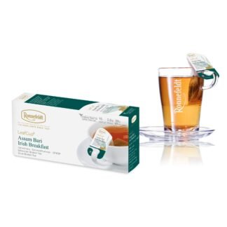 Opakowanie herbaty Ronnefeldt LeafCup Assam Bari Irish Breakfast obok szklanki z przygotowaną herbatą. Herbata Assam Bari Irish Breakfast to czarna herbata z mieszanką przypraw, oferowana w eleganckim pudełku z 15 torebkami herbaty, idealna do przygotowania aromatycznego napoju. Obok znajduje się przezroczysta szklanka z logo Ronnefeldt, ukazująca napój o bogatej, ciemnej barwie.