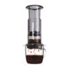 Zdjęcie czarnego zaparzacza AeroPress Clear Black, umieszczonego na szklance z zaparzaną kawą. Krople kawy spadają do kubka, ukazując proces parzenia metodą AeroPress, z przezroczystym czarnym korpusem urządzenia.