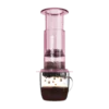 Zdjęcie różowego zaparzacza AeroPress Clear Pink, umieszczonego na szklance z zaparzaną kawą. Widoczna jest ekstrakcja kawy, której krople spadają do kubka, ukazując proces parzenia kawy metodą AeroPress.