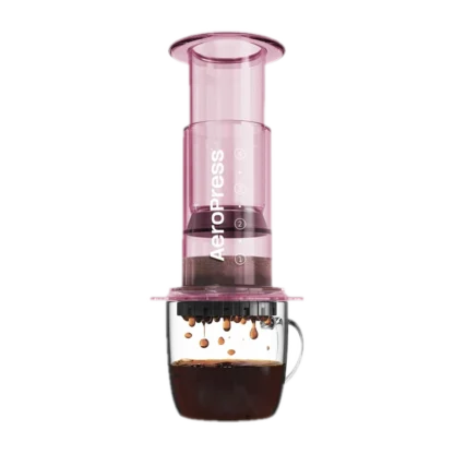 Zdjęcie różowego zaparzacza AeroPress Clear Pink, umieszczonego na szklance z zaparzaną kawą. Widoczna jest ekstrakcja kawy, której krople spadają do kubka, ukazując proces parzenia kawy metodą AeroPress.