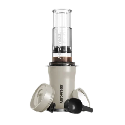 Zdjęcie kremowego ekspresu AeroPress Go Plus, w skład którego wchodzi cylindryczna komora do parzenia kawy, tłok z miarką, pokrywka podróżna oraz miarka do kawy. Urządzenie jest kompaktowe i idealne do przygotowywania kawy w podróży.