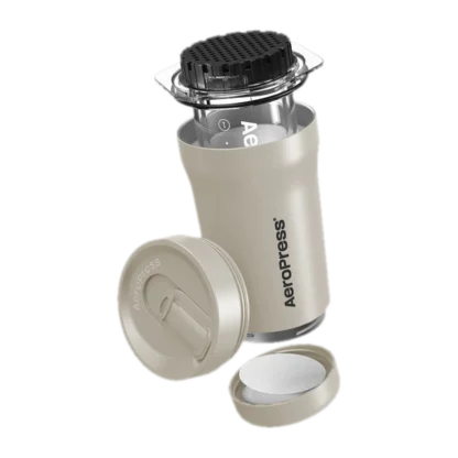 Zdjęcie złożonego zestawu AeroPress Go Plus w kolorze kremowym, w którym widoczna jest cylindryczna komora do parzenia kawy, przykryta nakładką z sitkiem, obok leży zamknięcie podróżne oraz pojemnik na filtr papierowy. Kompaktowy zestaw idealny do przygotowywania kawy w podróży.