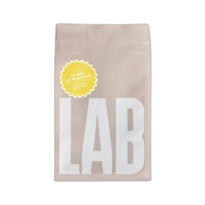 Opakowanie kawy speciality CoffeeLab Kolumbia Luis Marcelino Aji w minimalistycznym beżowym designie z dużym białym napisem "LAB". Wysokiej jakości ziarna pochodzące z Kolumbii charakteryzują się nutami pomarańczy, rodzynek i karmelowego likieru, tworząc wyjątkowy profil smakowy.