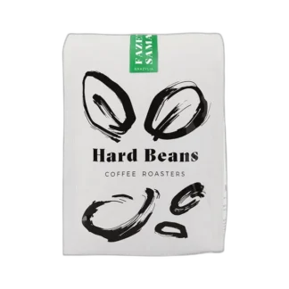 Białe opakowanie kawy Hard Beans Brazylia Samambaia Yellow Bourbon 500 g z czarnymi ilustracjami ziaren i zieloną etykietą, dostępne w sklepie z kawą specialty