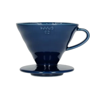 Elegancki ceramiczny dripper Hario V60-02 w głębokim kolorze indygo, idealny do precyzyjnego parzenia kawy metodą pour-over. Kultowy stożkowy kształt z wewnętrznymi żłobieniami zapewnia równomierną ekstrakcję, podkreślając pełnię smaku i aromatu ziaren.