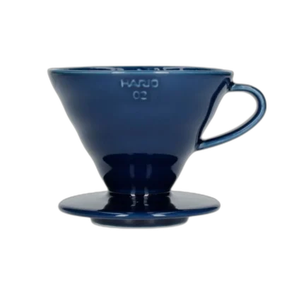 Elegancki ceramiczny dripper Hario V60-02 w głębokim kolorze indygo, idealny do precyzyjnego parzenia kawy metodą pour-over. Kultowy stożkowy kształt z wewnętrznymi żłobieniami zapewnia równomierną ekstrakcję, podkreślając pełnię smaku i aromatu ziaren.