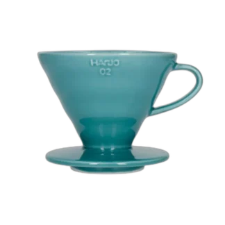 Stylowy ceramiczny dripper Hario V60-02 w turkusowym odcieniu, stworzony do precyzyjnego parzenia kawy metodą przelewową. Stożkowy kształt i spiralne żłobienia wewnętrzne zapewniają równomierną ekstrakcję, podkreślając głębię smaku świeżo mielonych ziaren.