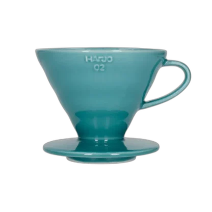 Stylowy ceramiczny dripper Hario V60-02 w turkusowym odcieniu, stworzony do precyzyjnego parzenia kawy metodą przelewową. Stożkowy kształt i spiralne żłobienia wewnętrzne zapewniają równomierną ekstrakcję, podkreślając głębię smaku świeżo mielonych ziaren.