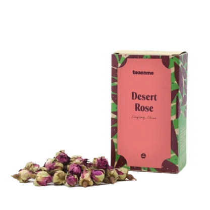 Opakowanie herbaty kwiatowej Teasome Desert Rose z regionu Xinjiang w Chinach, zawierające 50 g aromatycznych, suszonych pąków róż o intensywnie różowym kolorze. Produkt zaprezentowany jest w dekoracyjnym pudełku z motywem roślinnym, obok którego ułożono naturalne kwiaty przeznaczone do parzenia.