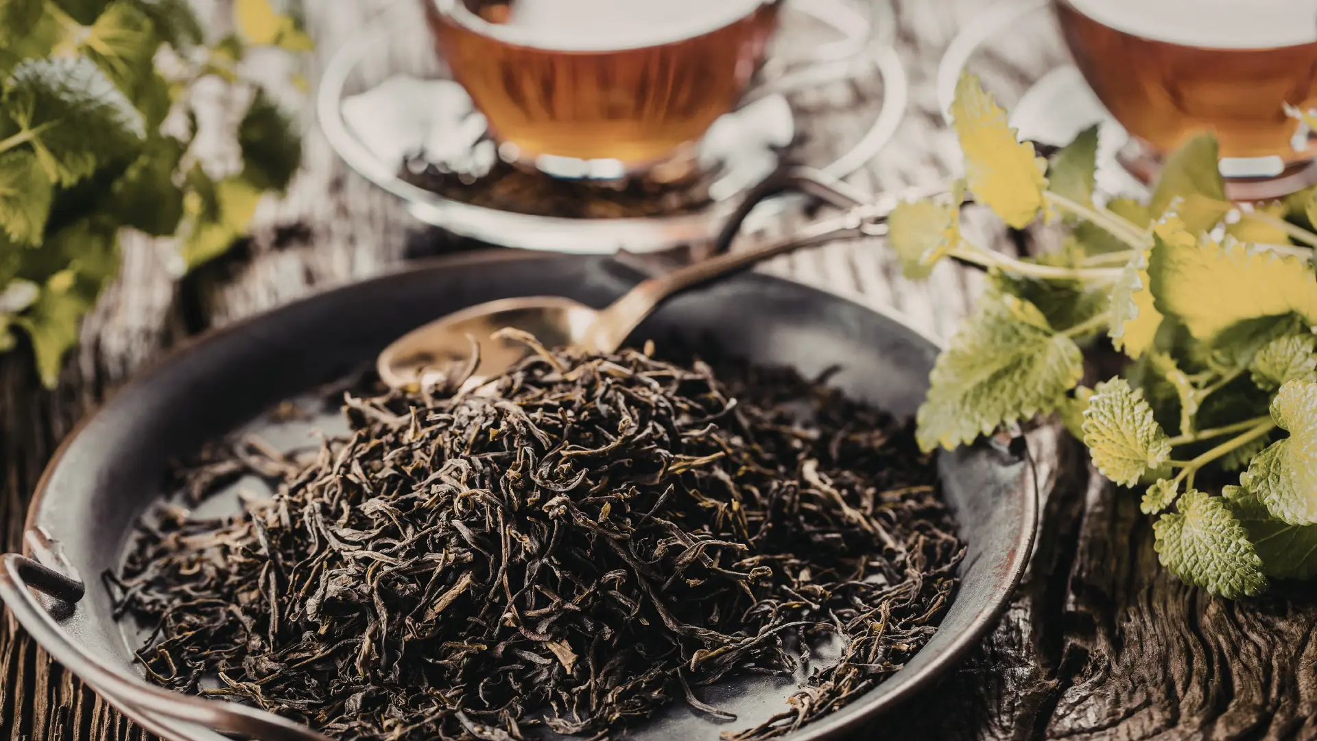 Herbata liściasta o głębokim aromacie na rustykalnym tle. Naturalne suszone liście i bursztynowy napar podkreślają jej wysoką jakość i smak.