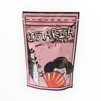 Opakowanie kawy Costarica Don Alexis w kolorze różowym, ozdobione ilustracją stylizowanej postaci. Wyjątkowy smak tej kawy z Costa Riki idealnie sprawdzi się dla miłośników wysokiej jakości napojów i akcesoriów do parzenia kawy.